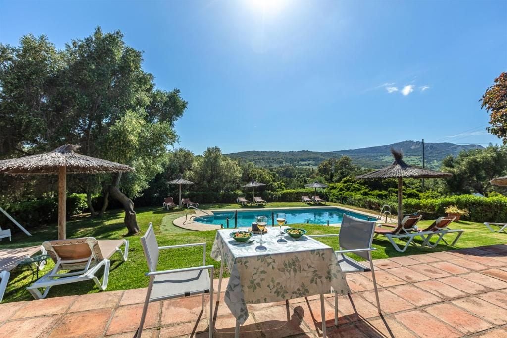 Un área de piscina con sillones de descanso, una mesa con mantel y sombrillas.