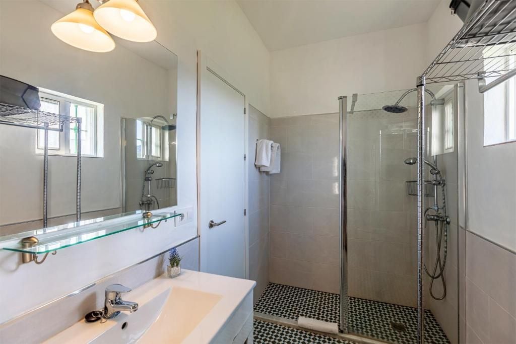 Une salle de bain avec une douche à parois de verre, un lavabo blanc et un miroir doté d’une étagère en verre.