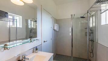 Une salle de bain avec une douche à parois de verre, un lavabo blanc et un miroir doté d’une étagère en verre.