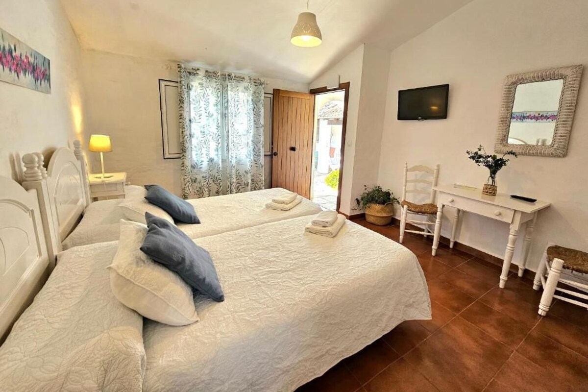 Quarto com duas camas, uma escrivaninha, uma cadeira, uma TV e um espelho.