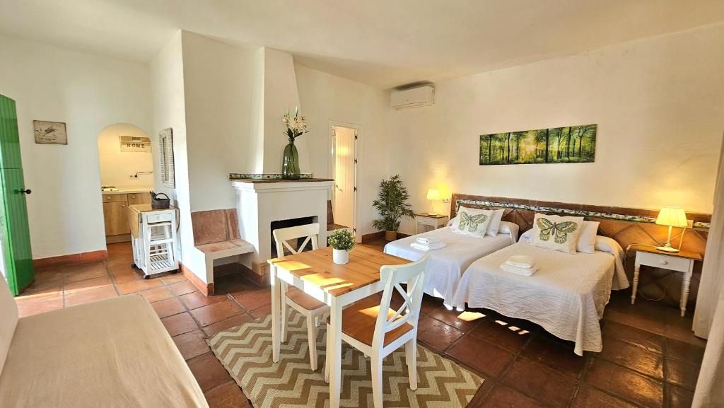 A hotel room with two beds, a dining table, a chair, a small kitchen area, and a living area with a painting on the wall.