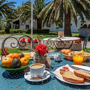 Disposição para um café da manhã ao ar livre com mesa, frutas, pão e bebidas.
