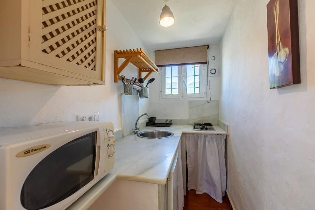 Een kleine keuken met een magnetron, spoelbak en een ophangrek voor keukengerei.