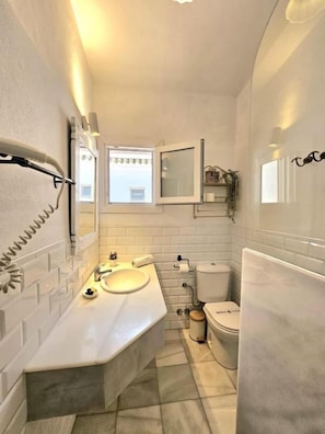 Casa de banho com lavatório branco, espelho e sanita.