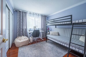 Huoneessa on kerrossänky, työpöytä, tuoli, säkkituoli ja ikkuna, jossa on verhot.