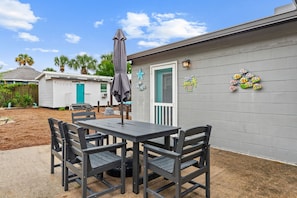 A patio with a table and chairs, a grey wall with decorative elements, and a blue door. - 3BR Coastal Getaway l Game Room l Outdoor Bar (Panama City Beach)