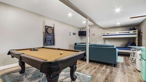 Una habitación con mesa de billar, sofá, litera y dardos.