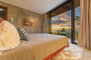 Un dormitorio con una cama grande, vistas al paisaje a través de ventanales y una obra de arte colgada en la pared.