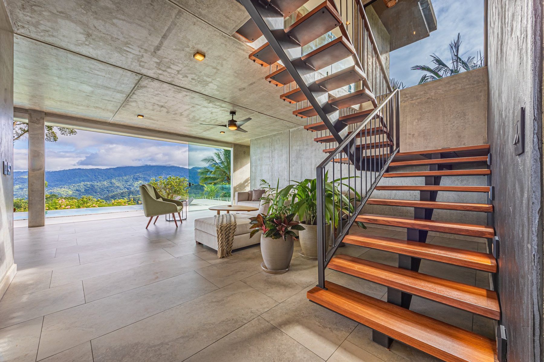 Un intérieur moderne avec un escalier en béton, un coin salon offrant une vue dégagée et une grande plante en pot.