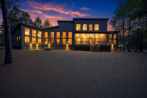 A modern two-story house with large windows and a gravel driveway. - Broken Bow Bliss · Private Heated Pool, Hot Tub & Arcade Game Room | Sleeps 12 (Broken Bow)