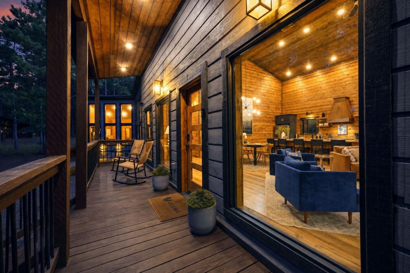 A wooden deck with a dining area and seating, a large window overlooking the interior, and a warm interior lighting.