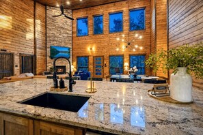 A modern kitchen with granite countertops, a black sink, and a dining area with a table set for four. - Broken Bow Bliss · Private Heated Pool, Hot Tub & Arcade Game Room | Sleeps 12 (Broken Bow)