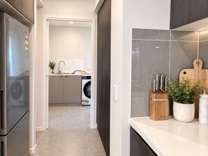Cocina moderna con lavadora integrada, refrigerador de acero inoxidable y encimera con cuchillos y una planta.