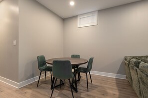 Ein Zimmer mit einem runden Tisch, vier Stühlen, einem Fenster mit Jalousien und einem Sofa.