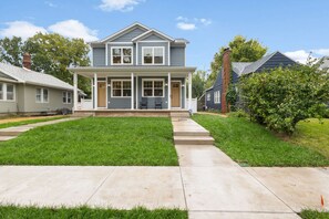 A two-story house with a front porch, a well-maintained lawn, and a clear sky. - Irish Victory House | 5BR/4BA (South Bend)