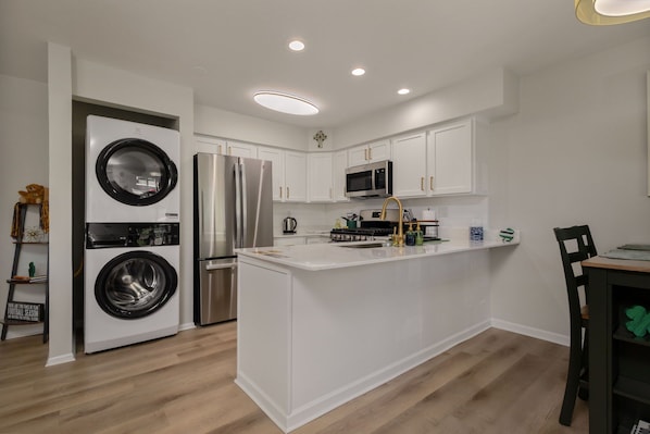 A compact kitchen with a built-in washer and dryer, stainless steel appliances, and a central island. - Luxury Legacy Retreat | Sleeps 10 | South Bend (South Bend)
