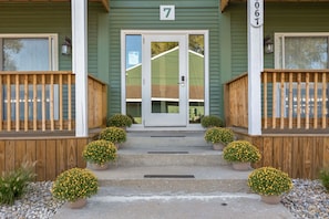 A two-story building with a green exterior, a white door, and a wooden porch with steps leading to the entrance. - Luxury Legacy Retreat | Sleeps 10 | South Bend (South Bend)