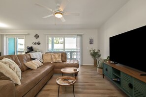 A living room with a brown leather sofa, two round wooden coffee tables, a ceiling fan, a television on a green cabinet, and a large window with a view of the outside. - Luxury Legacy Retreat | Sleeps 10 | South Bend (South Bend)