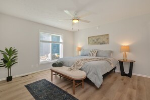 A bedroom with a bed, two bedside lamps, a ceiling fan, a window, a bench, and a potted plant. - Luxury Legacy Retreat | Sleeps 10 | South Bend (South Bend)