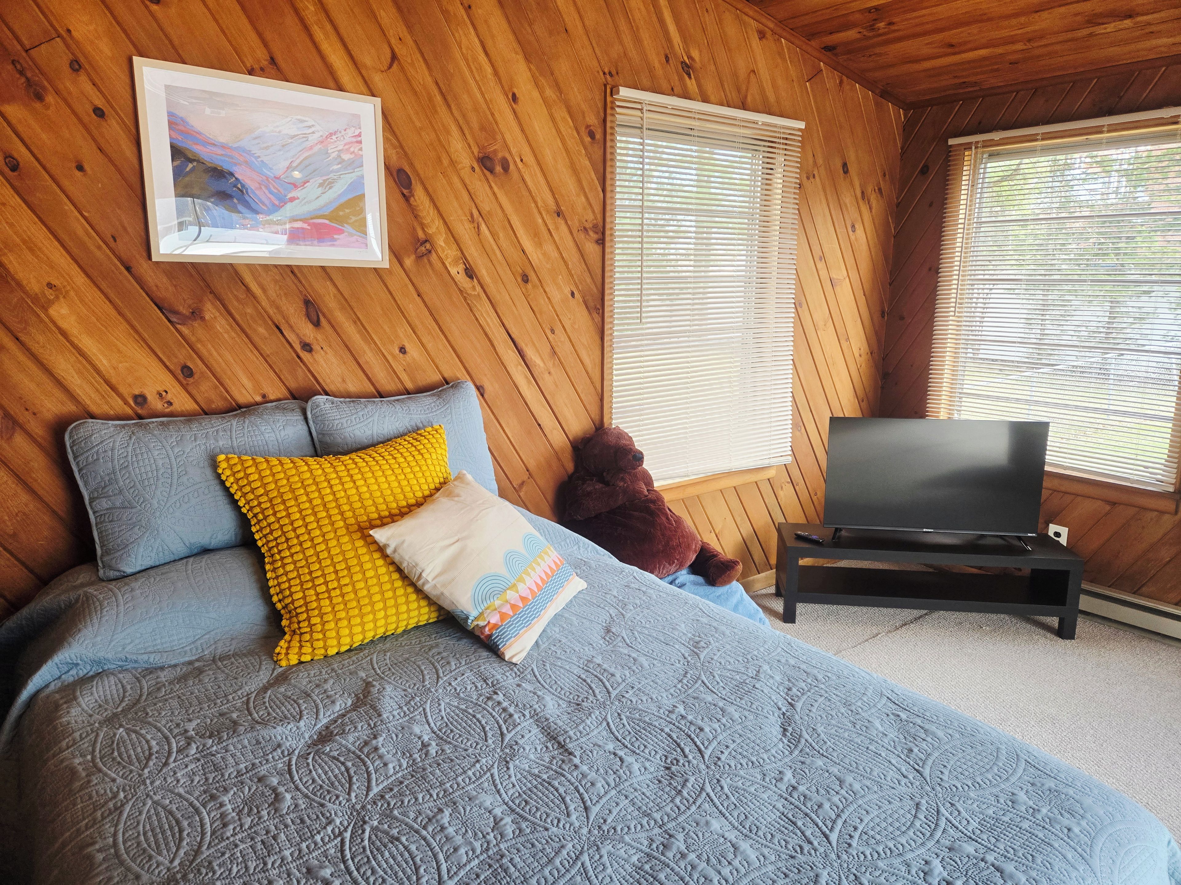 A wooden-paneled room with a bed, a television, and a teddy bear.