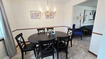 A dining area with a round table, six chairs, and a chandelier. There are two framed pictures on the wall.