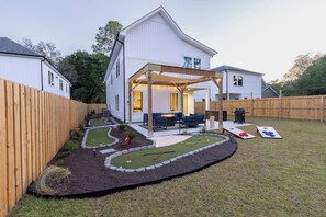 A residential backyard with a wooden deck, a small lawn, and a patio area with outdoor furniture. - Near Wrightsville, 3 Kings + Putting Green, Stylish Family & Group Getaway (Wilmington)