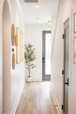 A hallway with a wooden floor, a potted plant, and framed artwork on the wall. - Near Wrightsville, 3 Kings + Putting Green, Stylish Family & Group Getaway (Wilmington)
