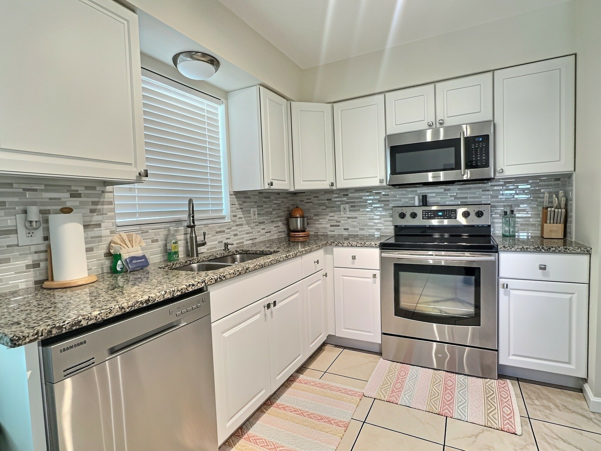 A modern kitchen with white cabinets, stainless steel appliances, a granite countertop, and a patterned rug.