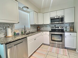 Una cocina moderna con armarios blancos, electrodomésticos de acero inoxidable, encimera de granito y alfombra estampada.