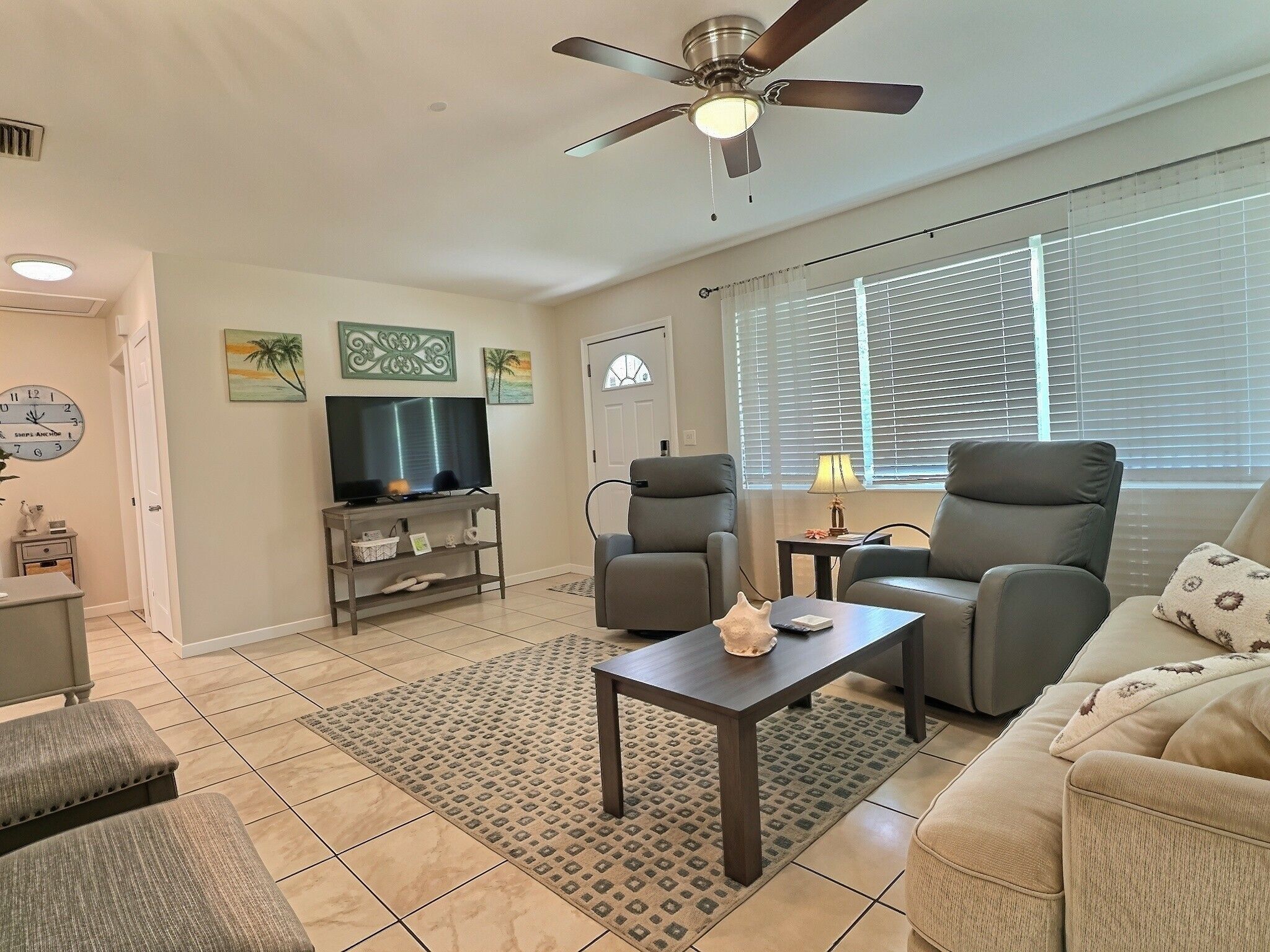 A living room with a ceiling fan, a television, two armchairs, a sofa, and a coffee table.