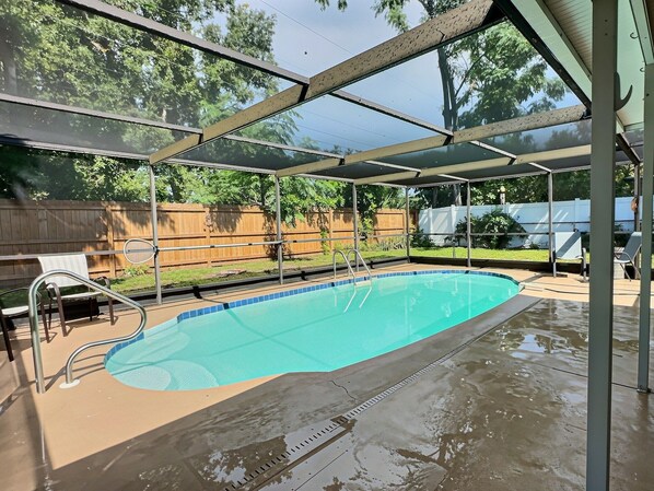 Una piscina con un área techada, barandillas metálicas y una valla de madera al fondo.