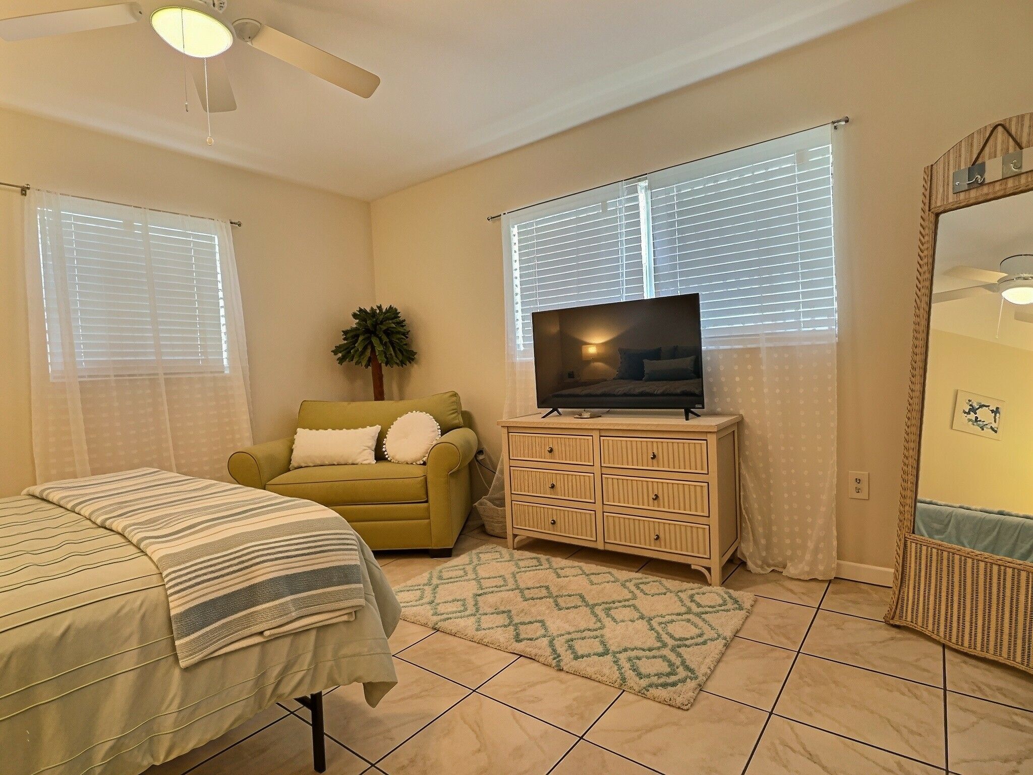 Un dormitorio con cama, un sofá, un televisor sobre un mueble de madera y un ventilador de techo.