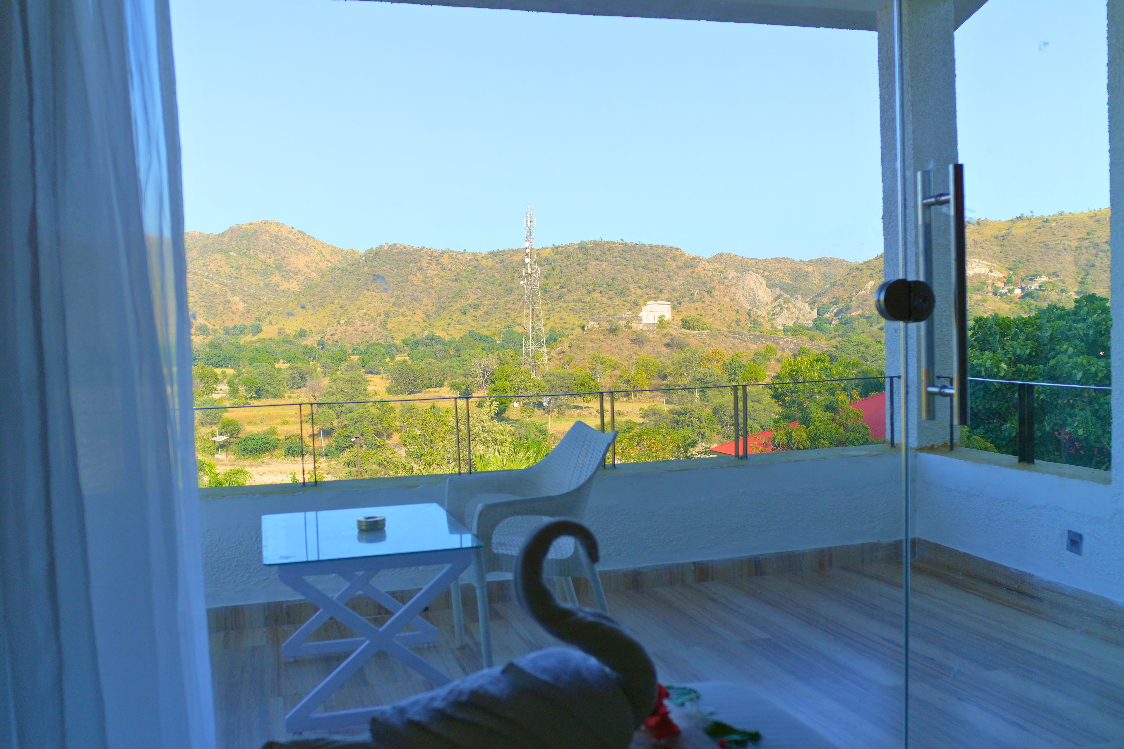 A balcony with a view of a hilly landscape, a table, and a chair.
