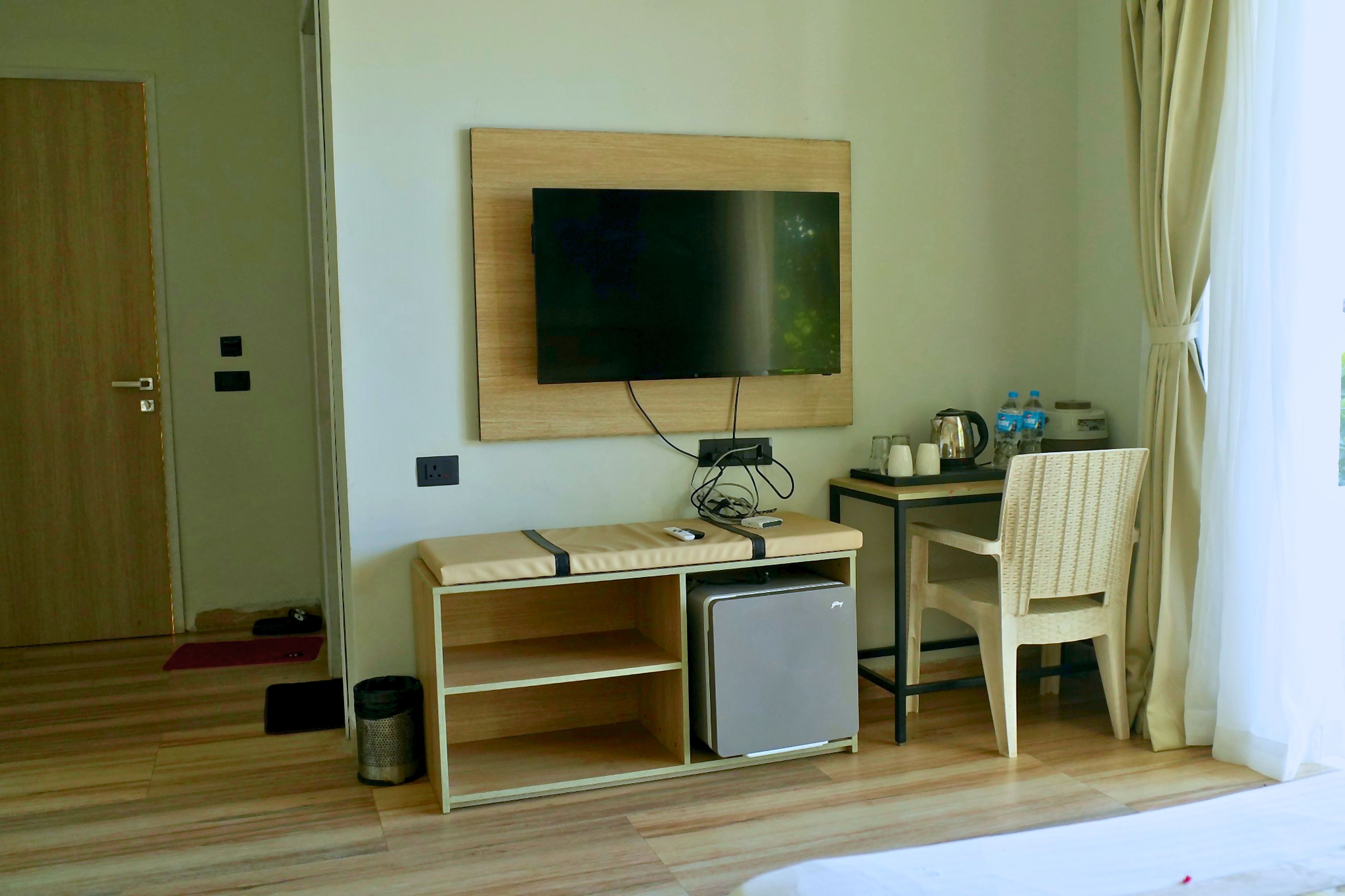 Habitación de hotel con televisión montada en la pared, un escritorio pequeño con una silla, un refrigerador pequeño y un cubo de basura.