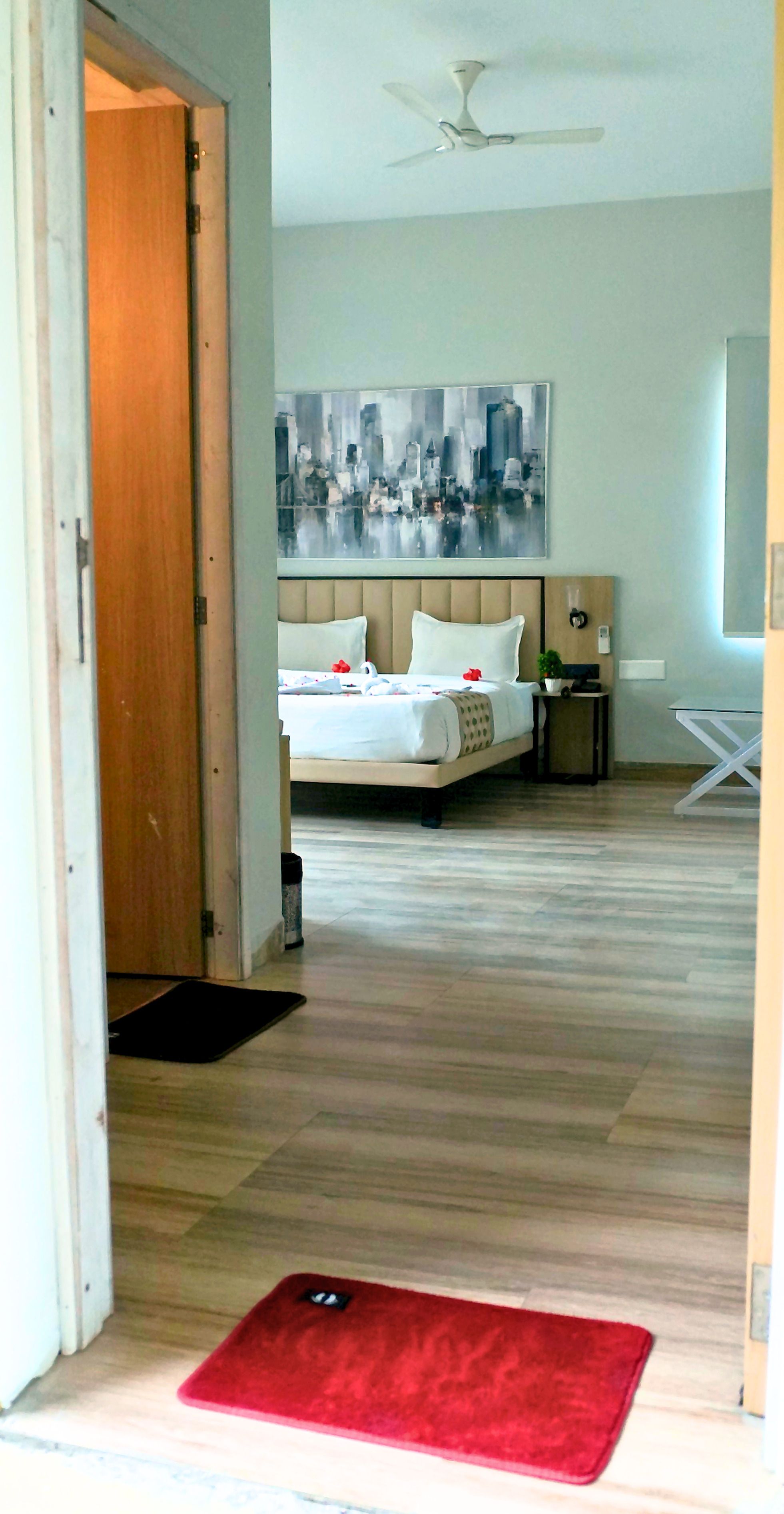 Una habitación de hotel con una cama, un ventilador de techo, un cuadro y una pequeña mesa con una planta.