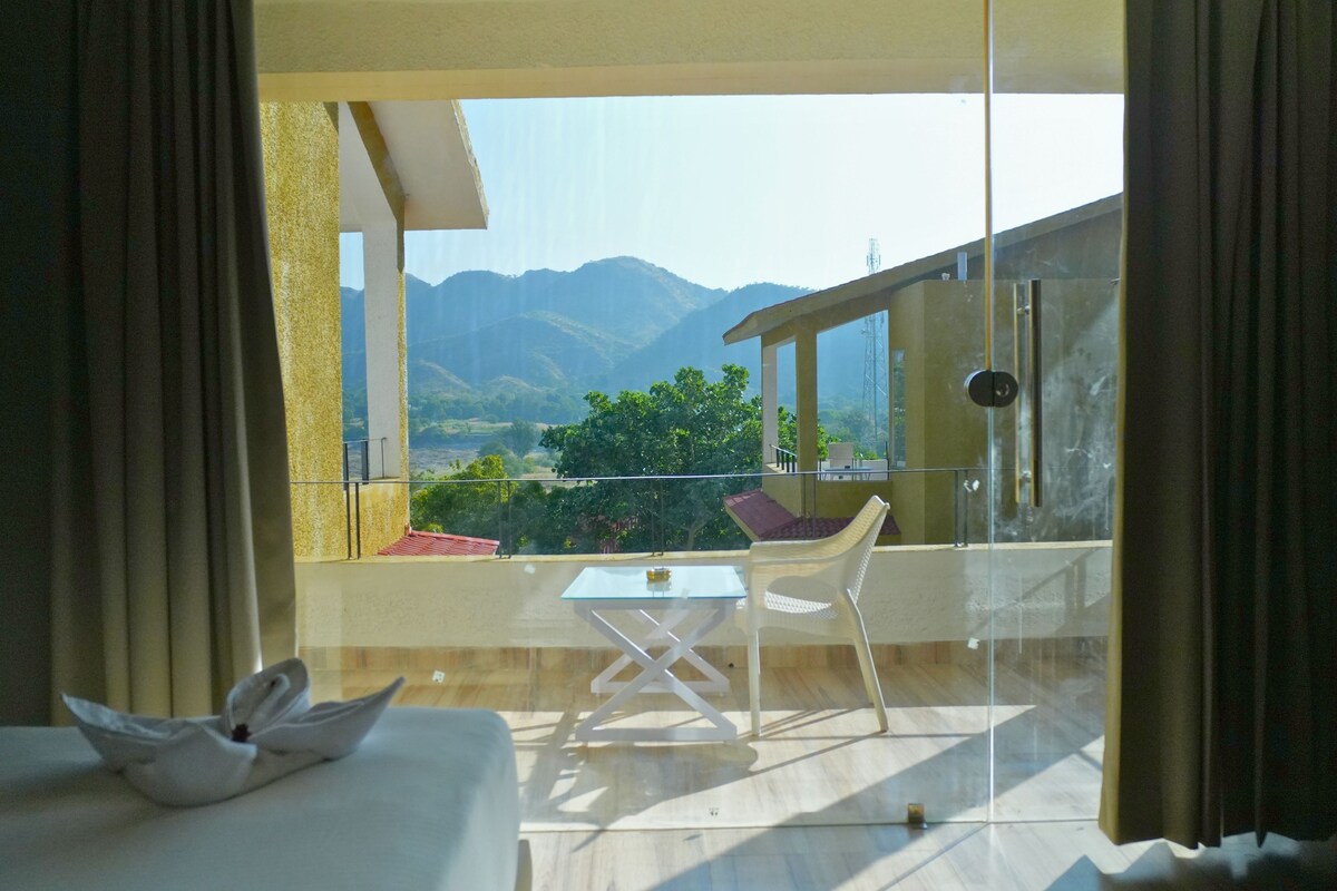 Un balcón con mesa y sillas, una cama con toalla, y vista a la montaña.