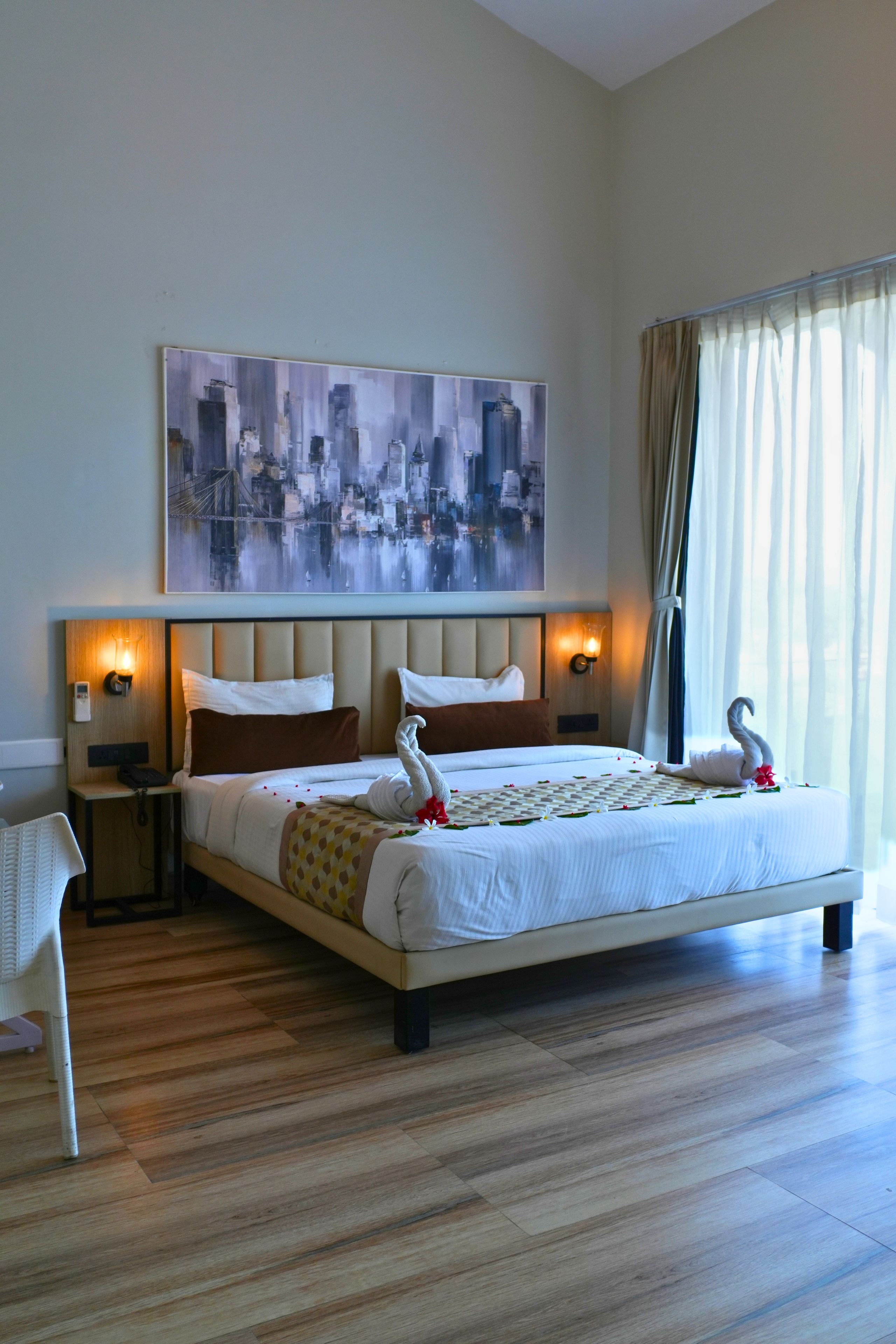 Habitación de hotel con una cama grande, un cuadro de paisaje urbano en la pared y una ventana con cortinas.