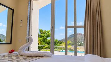 A hotel room with a bed, a swan-shaped towel, a view of a pool and mountains.