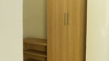 Una habitación con un armario de madera, un estante pequeño de madera y una escalera que baja a un nivel inferior.