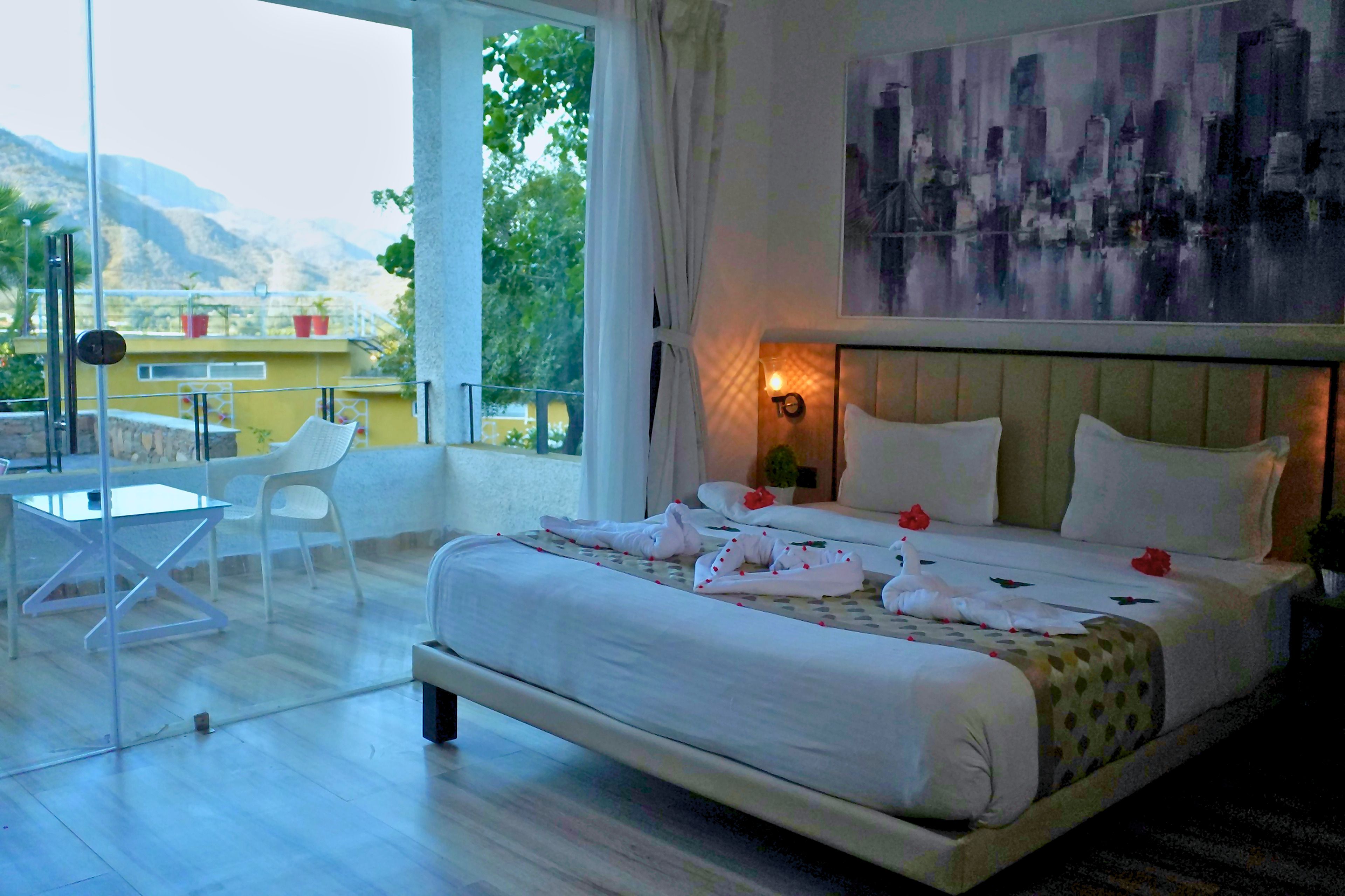 A hotel room with a bed, a chair, a table, and a view of the outdoors.
