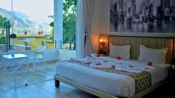 A hotel room with a bed, a chair, a table, and a view of the outdoors.