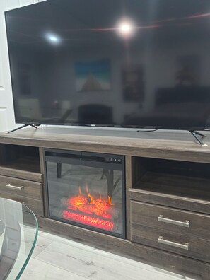 Un téléviseur à écran plat est posé sur un meuble de rangement en bois, et en dessous se trouve une cheminée à façade en verre.