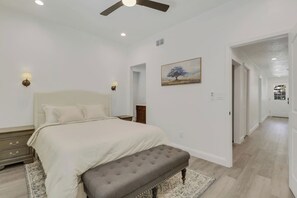 A bedroom with a bed, bedside tables, a bench, a ceiling fan, and a painting on the wall. - Walk to Historic Downtown | 3BD/2BA | Private Yard (St. Augustine)
