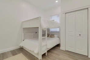 Ein Stockbett mit weißem Baldachin, ein Einzelbett mit Kissen, ein Kleiderschrank und ein Fenster mit Jalousien.