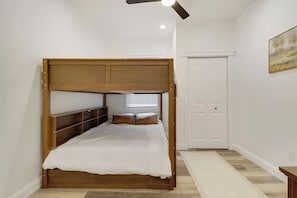 Une chambre avec un lit superposé, une armoire, un ventilateur de plafond et un tableau accroché au mur.