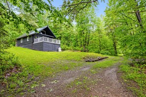 A cabin with a porch, surrounded by lush greenery and a gravel path.