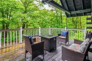 An outdoor deck with wicker furniture, a table, and a view of a forest.
