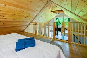 A bedroom with a wooden ceiling, a bed with white and blue bedding, and a view of a balcony.