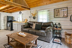A cozy cabin interior with a leather sofa, wooden coffee table, and a kitchen area.