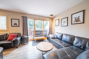 A modern living room with leather sofas, a wooden coffee table, and a sliding glass door leading to a balcony. - Alpine Retreat in Village Core, Sleeps 8 (Sun Peaks)